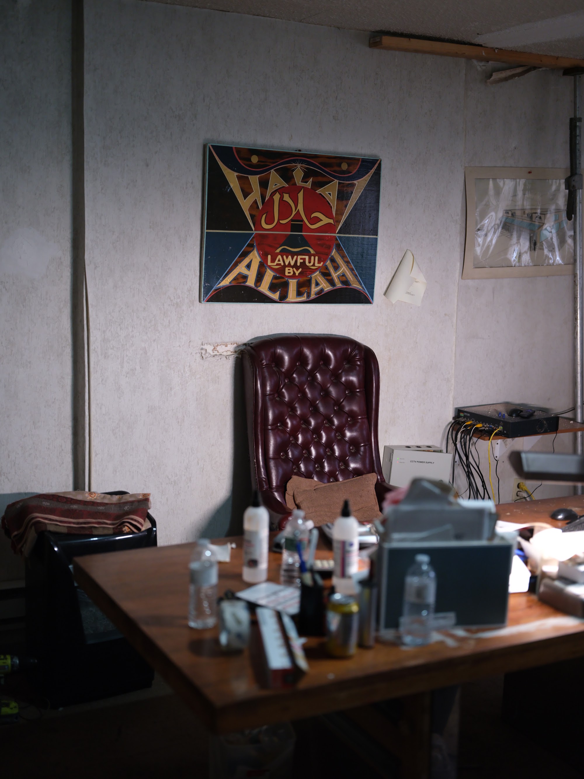 The back office. An empty leather chair beneath a hand-painted Halal Lawful By Allah sign